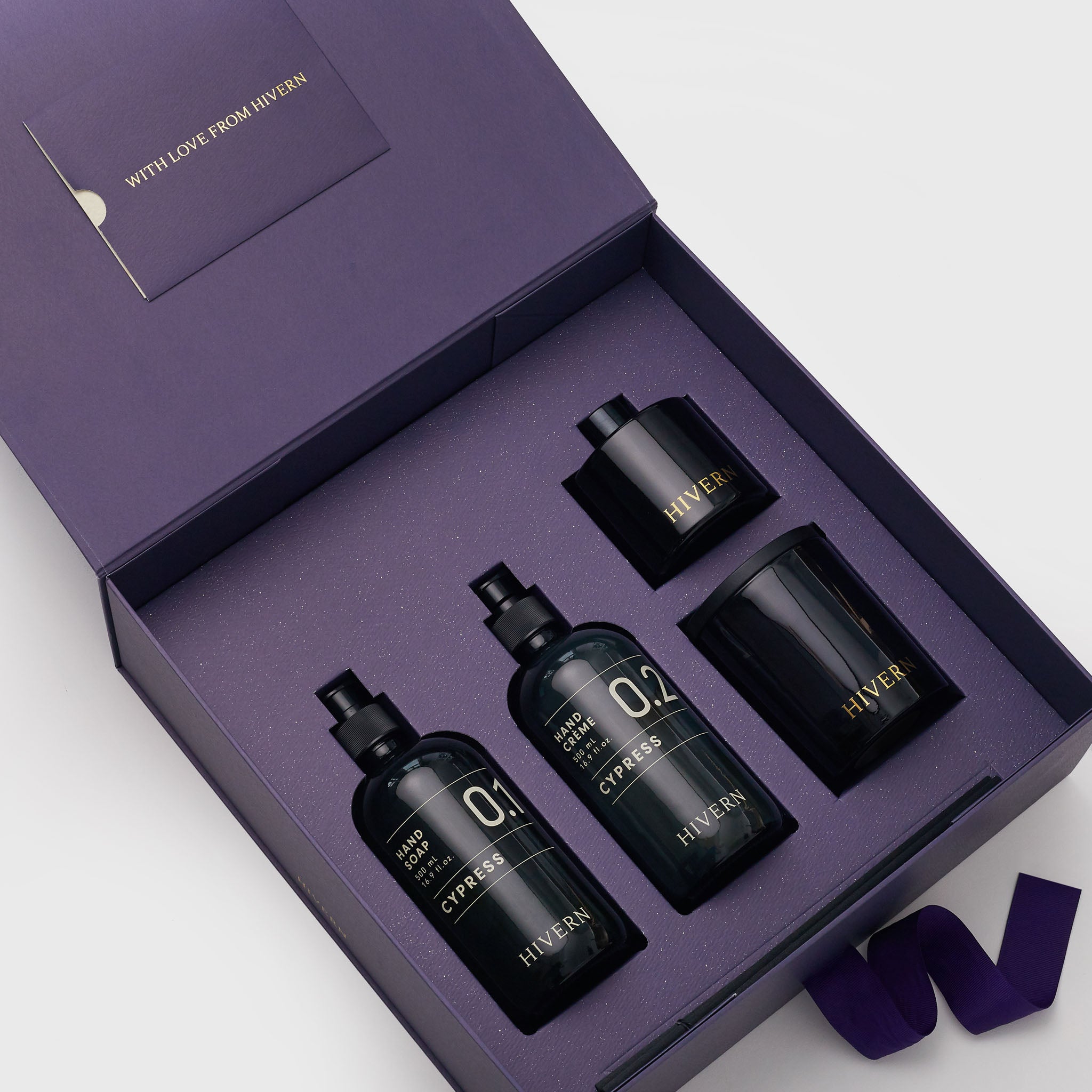 An open Hivern giftbox, displaying the contents of the gift set including: A glass pump bottle of Cypress Hand soap, a glass pump bottle of Cypress Hand Crème, a luxury glass fragrance diffuser and double wicked soya wax candle.