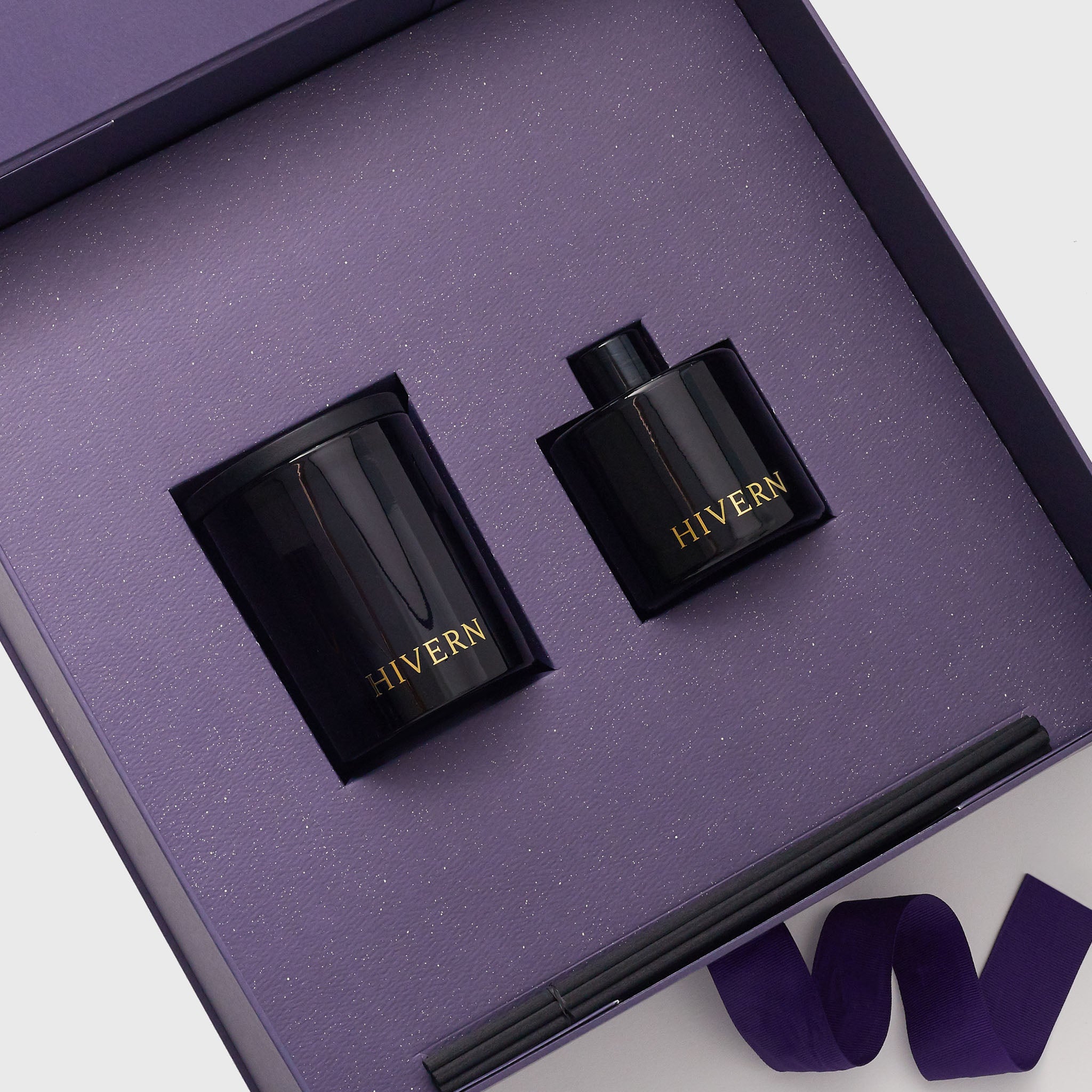 A Hivern luxury giftbox lays open, displaying it's contents, including a navy blue glass fragrance diffuser, emblazened with a gold foil Hivern logo and a navy blue glass enclosed double wick soya wax luxury fragrance candle.